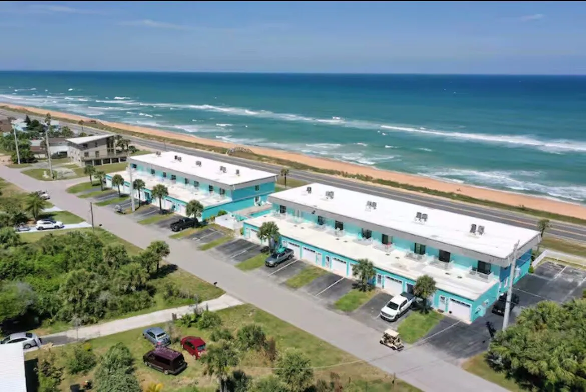 Aerial view of the teal Teal Octopus Beach Villa buildings on the Flagler Beach barrier island, with scenic A1A and the Atlantic surf running alongside