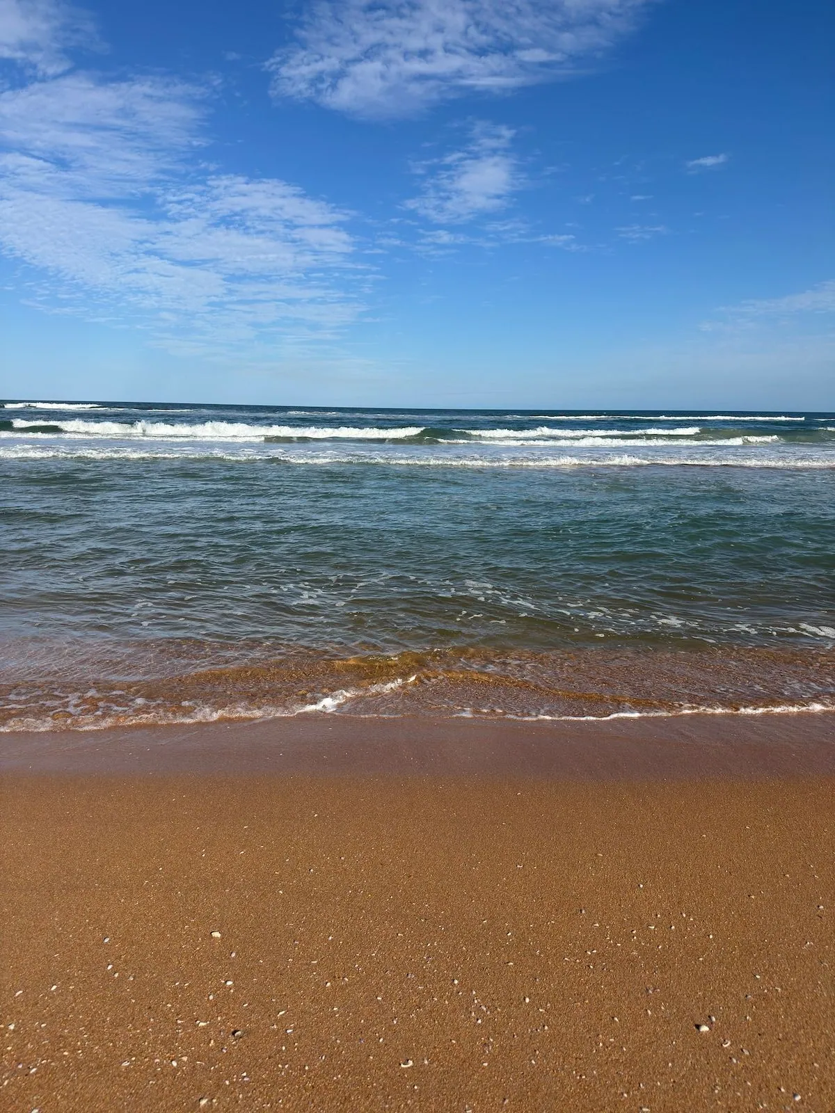 Gentle surf rolling onto the tawny sand of Flagler Beach beneath a bright blue sky