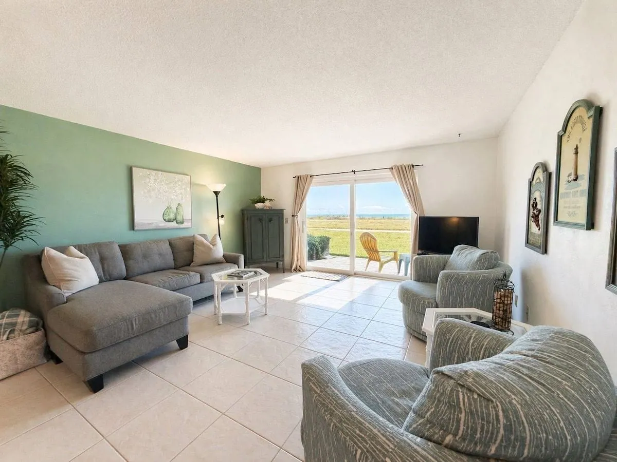 Living room with a sectional sofa bed, two coastal swivel chairs, smart TV and sliding doors opening to the lower balcony and ocean view