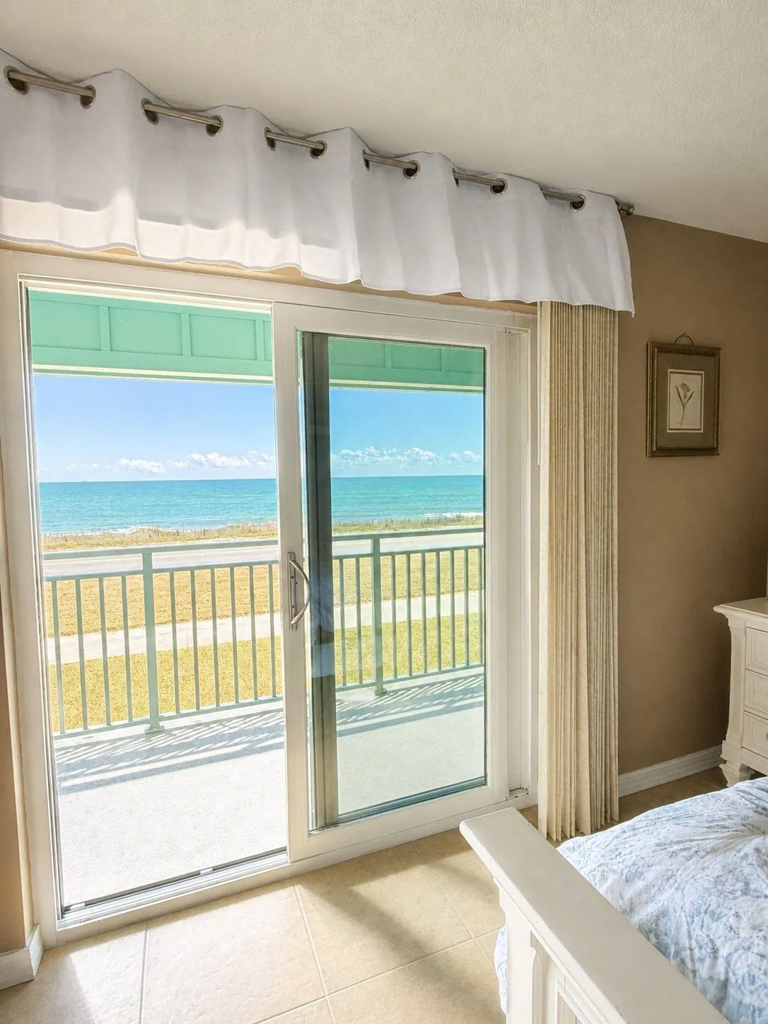Sliding glass doors in the master suite opening onto the teal oceanfront balcony, with the turquoise Atlantic beyond
