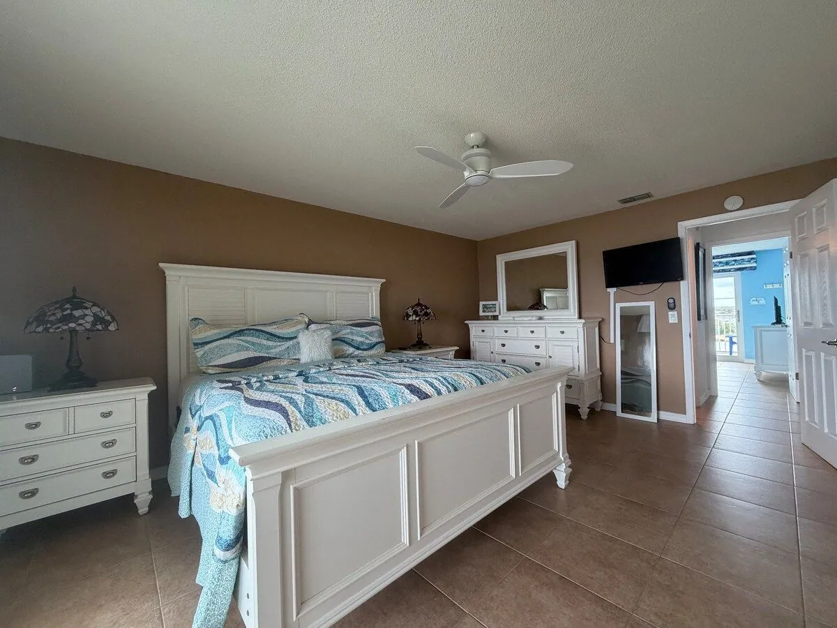 Wide view of the master suite showing the king bed, dresser, mirror and wall-mounted smart TV